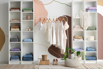 Stylish interior of light dressing room with female clothes and houseplant