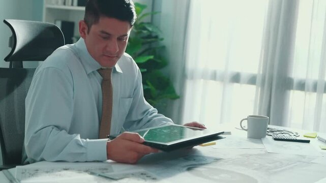Professional engineer looking at phone while working on tablet with green screen at meeting table with turbine engine or jet engine sketch design and various metal gear scatter around. Alimentation.