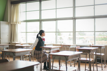 教室の中から窓の外を見る日本人の女子中学生