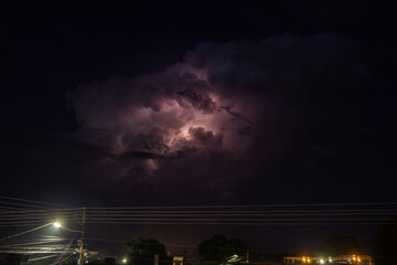 Lightning strike in the night sky with clouds and electricity pole.