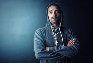 Man, arms crossed and hoodie in studio for training with thinking, workout and earphones by dark background. Person, music and mock up space to start exercise, pride and fitness routine for health