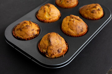 Freshly Baked Muffins in a muffin baking pan on dark background. Breakfast or dessert cupcakes viewed from a high angle in muffin tin