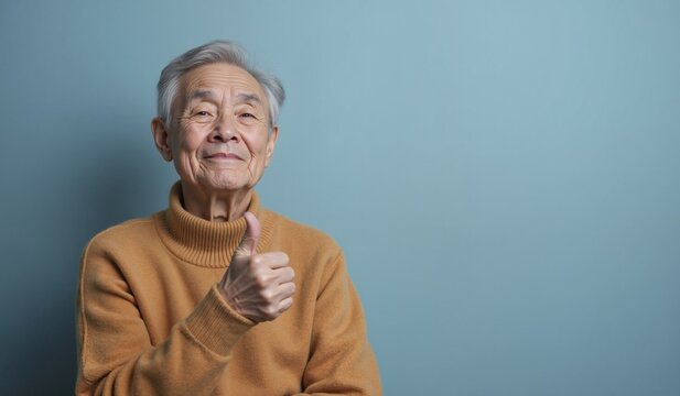 Senior Asian Man with Cheerful Expression Giving Thumbs Up Against Blue Background with Copy Space