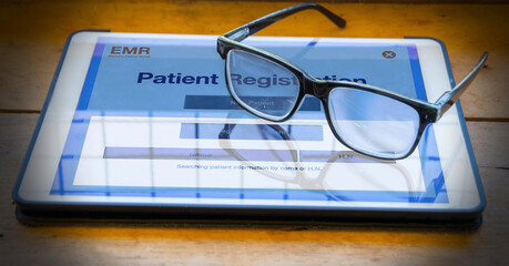 Eyeglasses are placed on digital tablet showing patient registration application menu via internet.