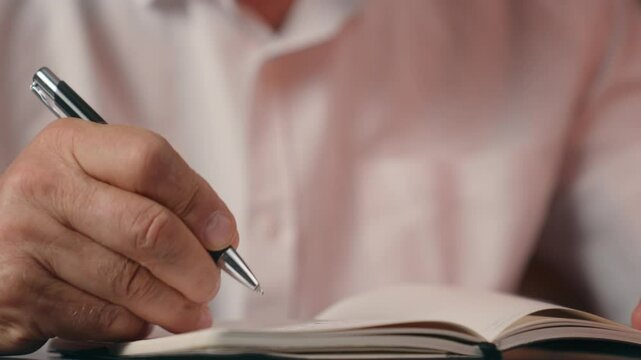 Close up hands holding pen writing writer journalist Caucasian old man senior home office indoors notebook businessman business working document author letter occupation note mature text paper male