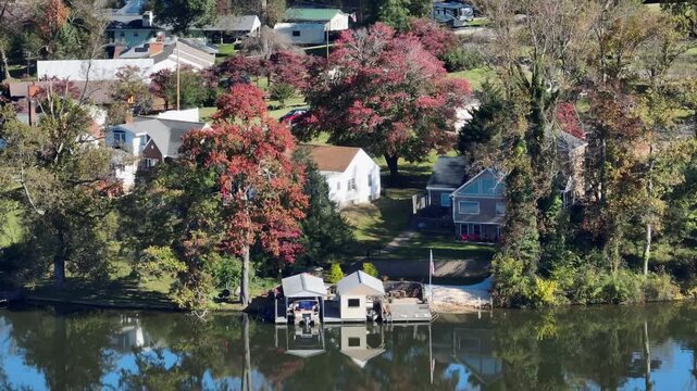 Aerial zoom shot of houses and private pier at Timber lake. Sunny autumnal day with colorful leaves on tree. Virginia, America.
