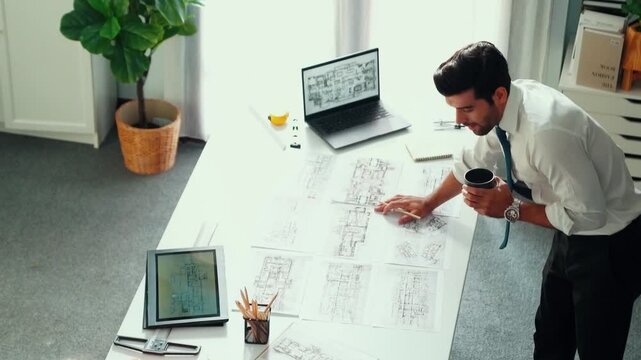 Architect engineer using laptop planning house design at office while sitting at meeting table with blueprint and equipment scatter around.Skilled civil engineer working at blueprint. Alimentation.