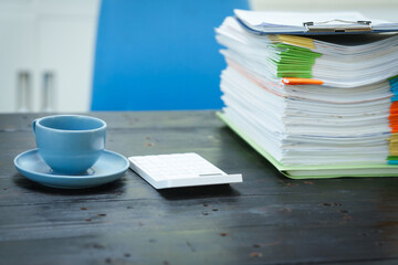 An empty office desk is cluttered with numerous documents and scattered coffee cups.The scene...