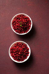 Two bowls of red lingonberries are placed on burgundy background. Top view