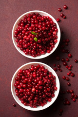 Two bowls of red lingonberries with scattered berries. Top view