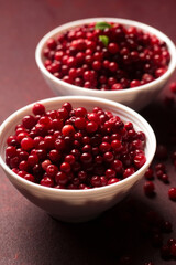 Two bowls of red lingonberries are placed on a burgundy background, close-up