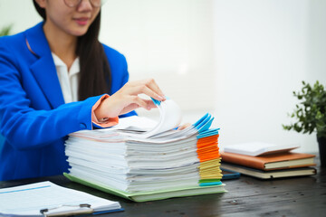 A young businesswoman works diligently at her office desk, checking documents and analyzing...