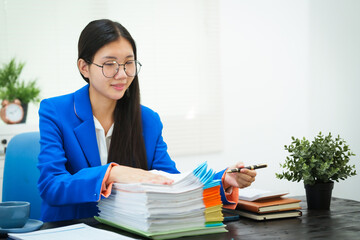 A young businesswoman works diligently at her office desk, checking documents and analyzing finances. She focuses on strategic planning to ensure the success and growth of her business