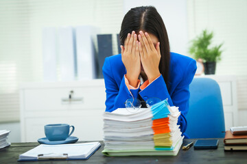A businesswoman sits at her desk in the office, exhausted and stressed from checking company documents. She suffers from headaches and anxiety due to being overloaded with work and prolonged sitting