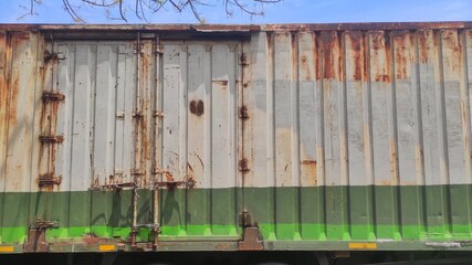 An old, weathered metal container door shows signs of rust and fading paint. The lower half is painted green with a bright green stripe, contrasting with the worn grey surface above.