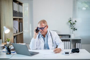 Senior doctor talking on the phone and taking notes in medical office