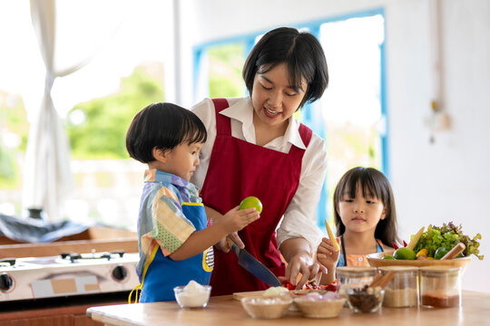 Happy asian family of mother and children preparing ingredients for cooking dinner in kitchen