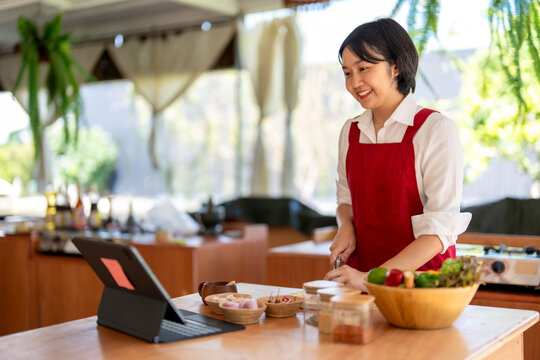 Asian woman learning cooking online using digital tablet in kitchen - Powered by Adobe