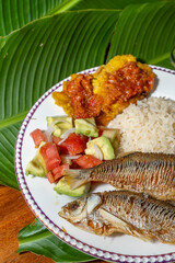 Exquisite Colombian dish with fish, coconut rice, salad and plantain with orange juice on a wooden table. Colombian gastronomy, typical dish.