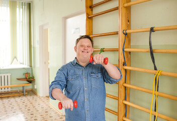 A man with Down syndrome is smiling and working out with dumbbells in a gymnasium