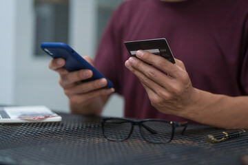 A businessman sits at a table, using his credit card to make an online payment on his laptop. He enjoys a lifestyle of frequent travel, shopping, and smart financial habits for wellness