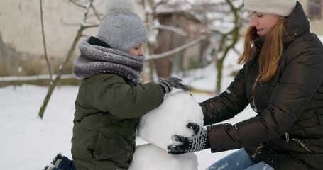Mother and child building a snowman outdoors in winter