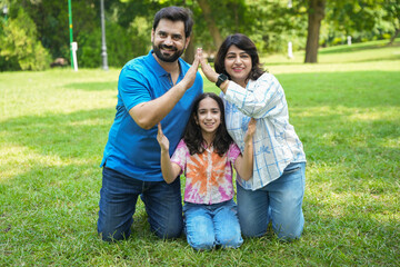 Happy indian family making the home sign with hands in summer park or garden. New house purchase,...