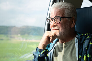 Pensive bearded old senior man sitting on train, savoring time spent on the journey, looking out of...