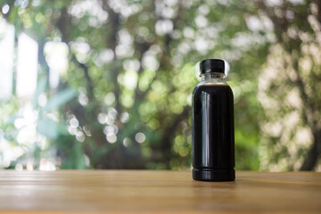 Black coffee in a bottle with bottle. Cold summer drink on a nature background with copy space