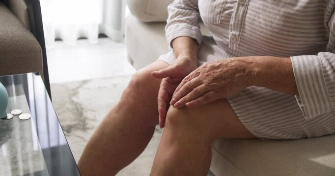 Top view of a pensioner's hands rubbing a popliteal or synovial cyst, a fluid-filled swelling that forms on the back of the knee. Popliteal cyst, fluid in joint. Damaged knee joint of an elderly woman