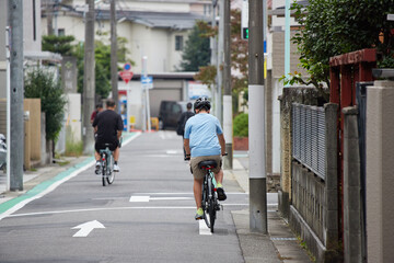 昼の住宅地の道路で自転車を乗る男性の姿