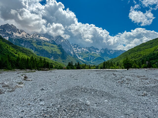 Vast field of rocks from dried riverbank with vista on majestic mountain massif Zhaborret, Albanian...