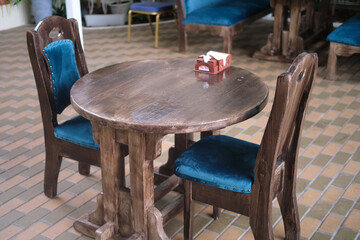 Rustic wooden table with two chairs featuring blue velvet cushions in a cafe setting. Indoor seating arrangement for dining. Casual dining and hospitality concept.
