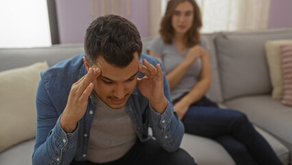 Fototapeta premium Man stressed sitting on couch with woman in living room, expressing relationship issues at home.
