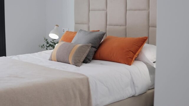 Camera moving through luxurious bedroom, showing comfortable bed with cushions and pillows, bedside table, and lamp