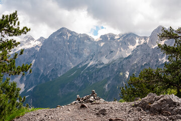 Obraz premium Breathtaking alpine landscape with trail leading to rocky outcrop. Small cairn of stones is piled at the edge offering panoramic view of mountain ridges of Albanian Alps (Accursed Mountains), Albania