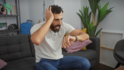 A surprised bearded man in a living room checking the time on his wristwatch, with a cactus decor...