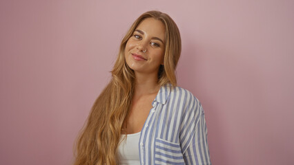 Fototapeta premium Beautiful blonde woman posing over isolated pink background, wearing a white tank top and striped shirt, showcasing an attractive smile and long hair, appearing confident and cheerful
