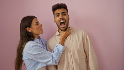 Woman holding man's neck against pink wall with humorous expression, creating a playful moment...