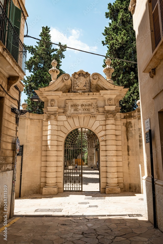 Wall mural Stone archway with intricate carvings and iron gate in a sunny European street in Palma de Mallorca