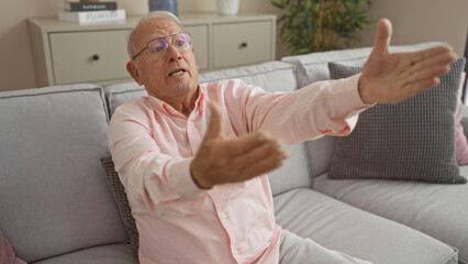 Elderly caucasian man gesturing passionately while sitting on a sofa in a cozy living room, displaying expressive communication in a home setting.