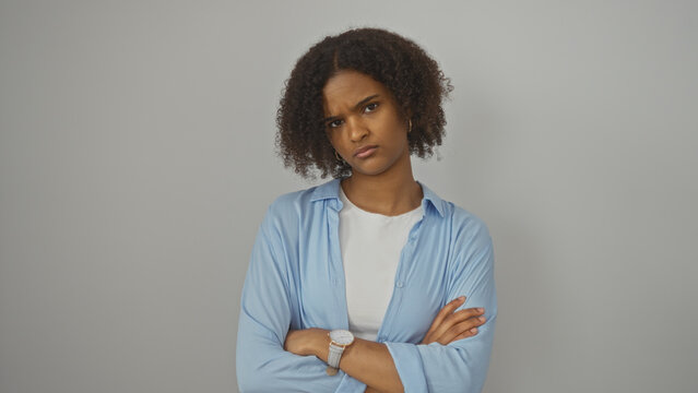 A beautiful young african american woman with curly hair stands with crossed arms against an isolated white background.