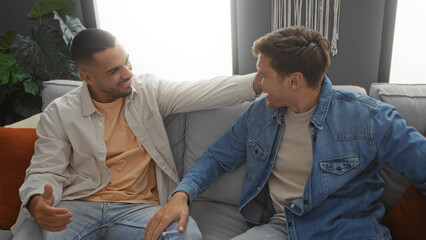 Fototapeta premium Men friends laughing together on a cozy couch in a modern apartment living room enjoying an indoor relaxed moment