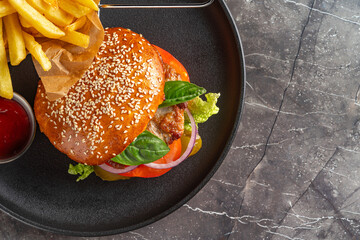 Close up of burger with french fries and ketchup on black plate