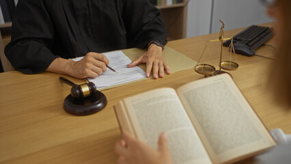 Judge signing a document in an office with a gavel and scales as a lawyer reads a book