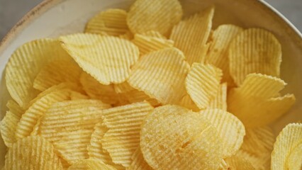 Closeup of yellow crispy potato chips in a bowl, showcasing their texture and freshness.