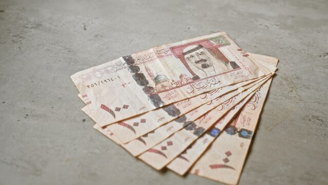 Saudi arabian riyals banknotes spread on a concrete surface, highlighting local currency details in a simple, financial setting.