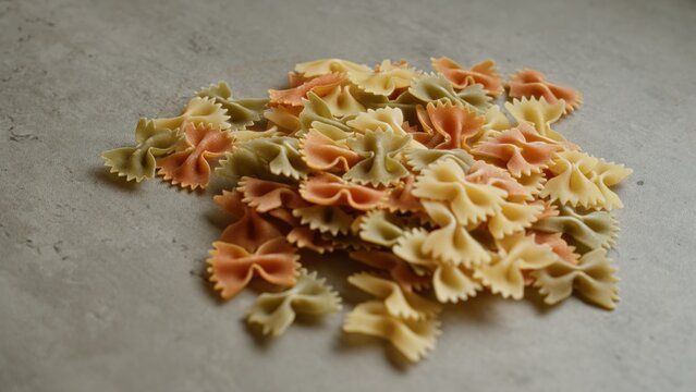 Colorful bowtie pasta scattered on a concrete surface in a close-up shot, showcasing its variety and texture.