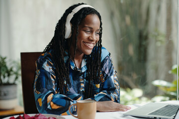 African American woman smiling while listening to music on headphones, sitting at a table. Vibrant...