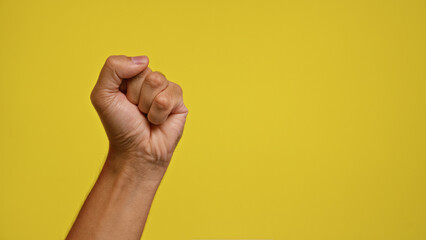 Man's hand making a fist against a vibrant yellow background signifying strength and determination